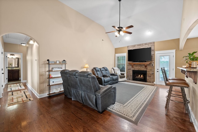 living room with a fireplace, baseboards, ceiling fan, arched walkways, and dark wood finished floors
