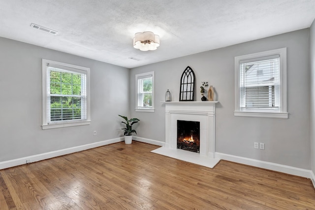 unfurnished living room with visible vents, wood finished floors, baseboards, a textured ceiling, and a fireplace with flush hearth