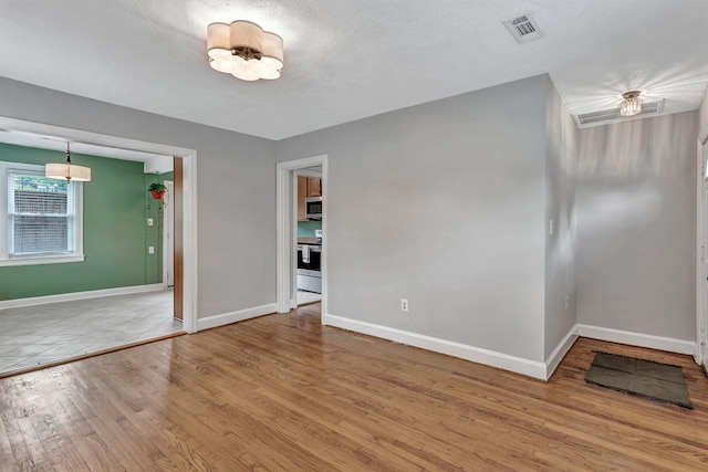 spare room with baseboards, a notable chandelier, wood finished floors, and visible vents