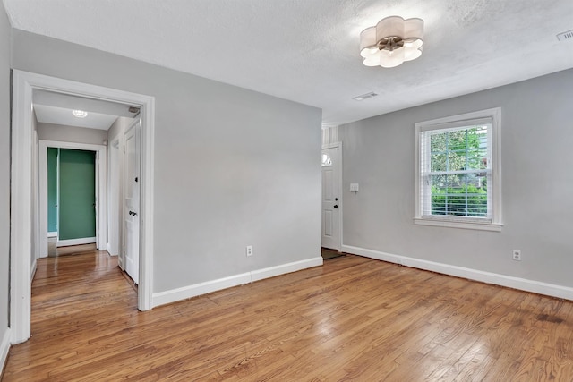 unfurnished room with a textured ceiling, baseboards, visible vents, and light wood-style flooring