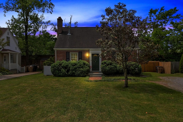 cape cod home featuring brick siding, fence, a yard, and a chimney