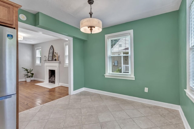 unfurnished dining area featuring baseboards, a fireplace with flush hearth, and light tile patterned floors