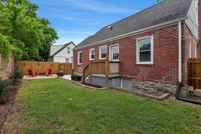 rear view of house with a fenced backyard, brick siding, a shingled roof, a lawn, and an outdoor fire pit