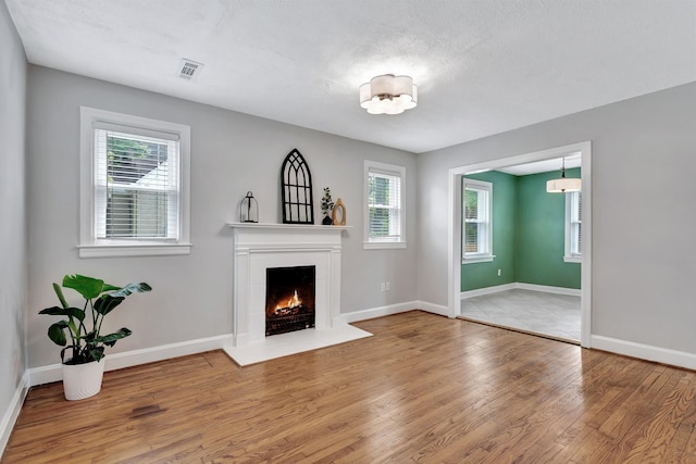 unfurnished living room featuring baseboards, a lit fireplace, wood finished floors, and visible vents