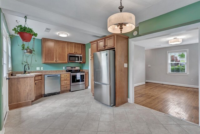 kitchen featuring brown cabinets, a sink, light tile patterned floors, decorative light fixtures, and stainless steel appliances