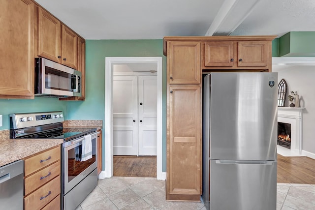 kitchen featuring baseboards, a lit fireplace, light countertops, appliances with stainless steel finishes, and light tile patterned floors