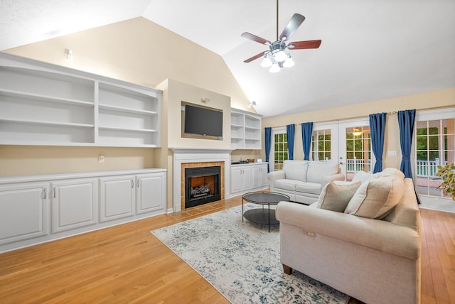 living room with a fireplace, high vaulted ceiling, light wood-type flooring, french doors, and a ceiling fan