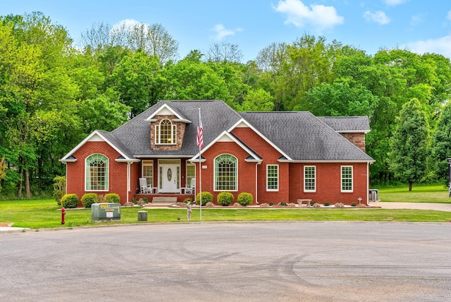 view of front of property featuring roof with shingles, a front yard, a porch, and brick siding