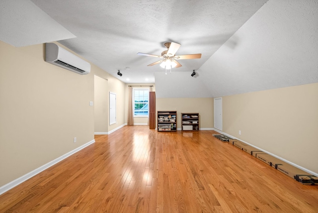 additional living space with light wood-style floors, baseboards, ceiling fan, an AC wall unit, and a textured ceiling