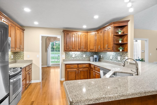 kitchen with brown cabinets, open shelves, appliances with stainless steel finishes, a sink, and light wood-style flooring