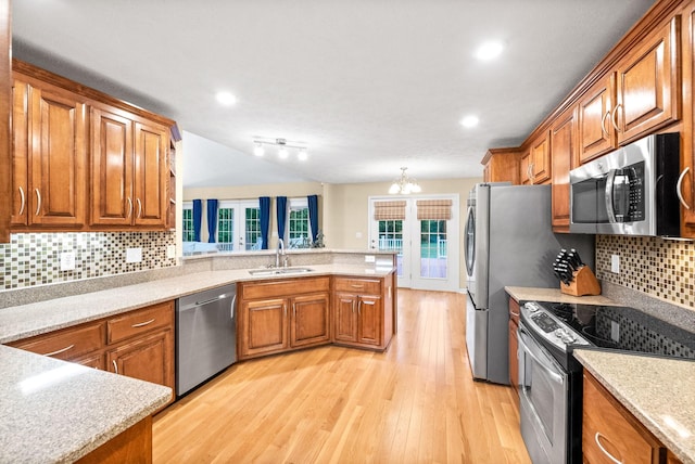 kitchen with brown cabinetry, light wood-type flooring, a sink, a peninsula, and stainless steel appliances