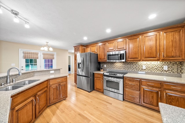 kitchen featuring appliances with stainless steel finishes, brown cabinets, a sink, light wood finished floors, and a chandelier