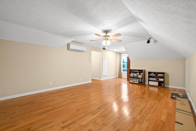 bonus room featuring a textured ceiling, ceiling fan, light wood-style floors, and a wall mounted air conditioner
