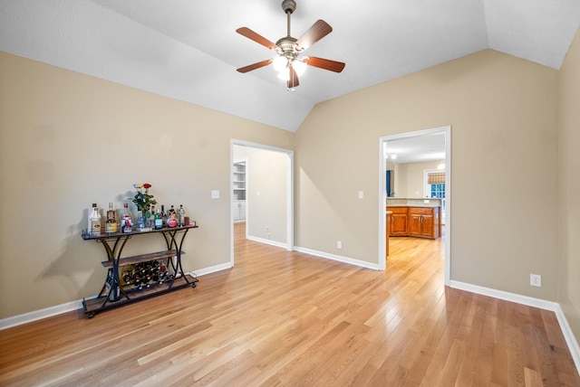 unfurnished room featuring baseboards, a ceiling fan, vaulted ceiling, and light wood finished floors
