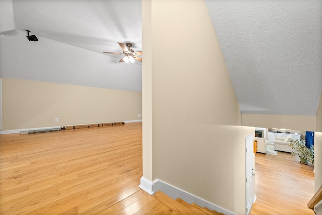 additional living space featuring baseboards, ceiling fan, vaulted ceiling, and light wood-type flooring