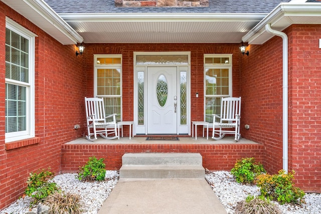 entrance to property featuring roof with shingles, covered porch, and brick siding
