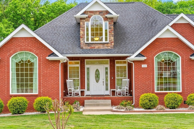 view of front facade with a shingled roof, a front lawn, and brick siding