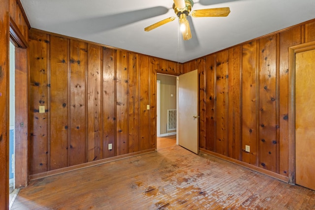 unfurnished room featuring visible vents, a ceiling fan, wooden walls, and hardwood / wood-style flooring