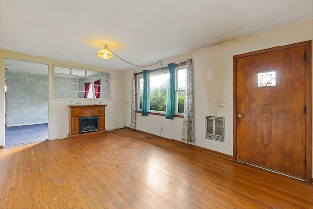 unfurnished living room with a fireplace with raised hearth, baseboards, heating unit, and wood finished floors