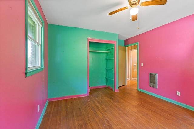 unfurnished bedroom with a closet, heating unit, wood finished floors, baseboards, and ceiling fan