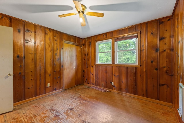spare room featuring wooden walls, ceiling fan, baseboards, and wood finished floors