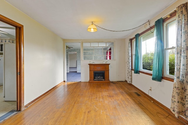 unfurnished living room featuring a ceiling fan, visible vents, baseboards, a fireplace with raised hearth, and light wood finished floors