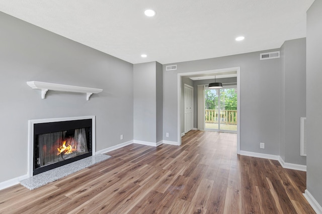 unfurnished living room with visible vents, baseboards, wood finished floors, and a warm lit fireplace