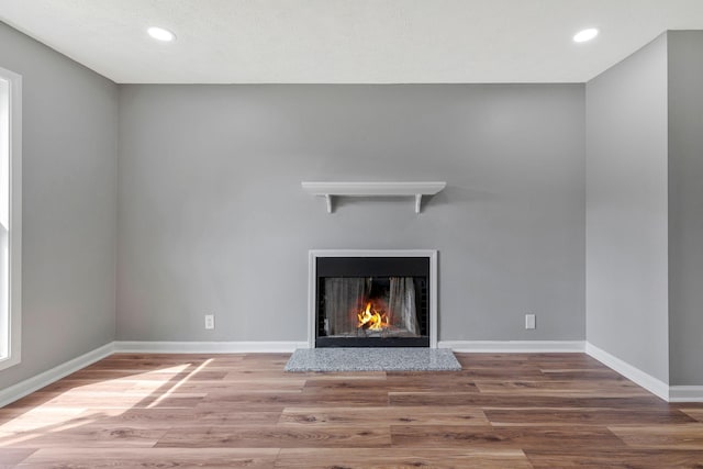 interior details with recessed lighting, a warm lit fireplace, and wood finished floors