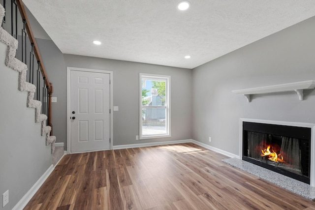 unfurnished living room featuring wood finished floors, baseboards, a textured ceiling, and stairs