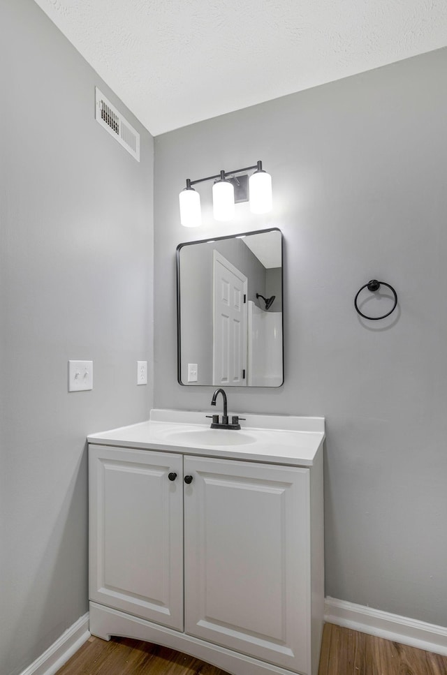 bathroom with baseboards, vanity, wood finished floors, and visible vents