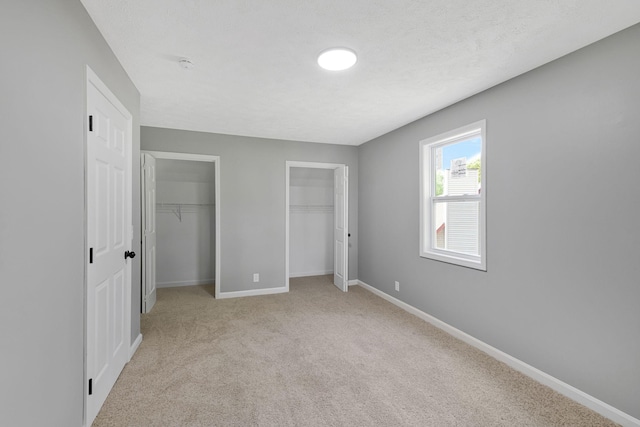 unfurnished bedroom with light colored carpet, baseboards, and multiple closets