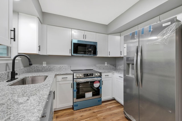 kitchen with light stone countertops, white cabinetry, a sink, light wood finished floors, and stainless steel appliances