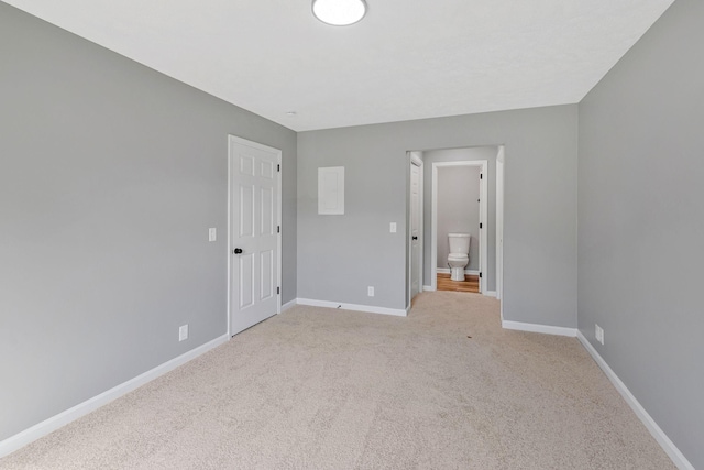 unfurnished bedroom with baseboards, light carpet, and ensuite bathroom