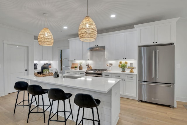 kitchen featuring crown molding, a breakfast bar, a sink, stainless steel appliances, and under cabinet range hood