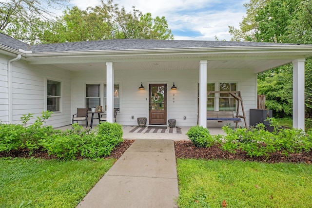view of exterior entry featuring a porch, roof with shingles, and a yard