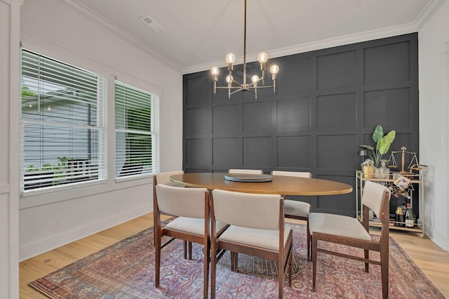 dining space featuring crown molding, visible vents, a decorative wall, light wood-style floors, and a chandelier
