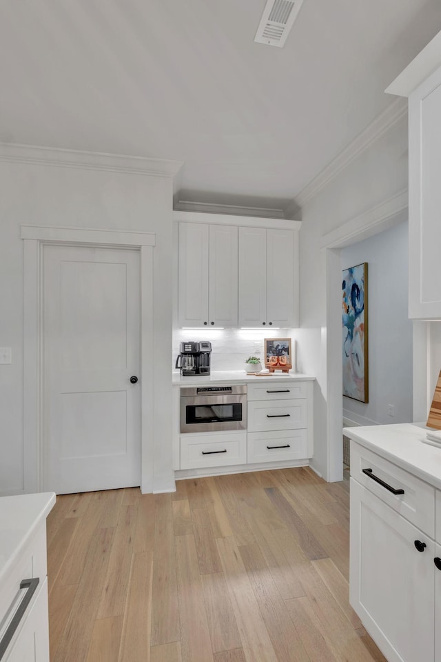 kitchen featuring ornamental molding, oven, light wood-type flooring, light countertops, and white cabinetry