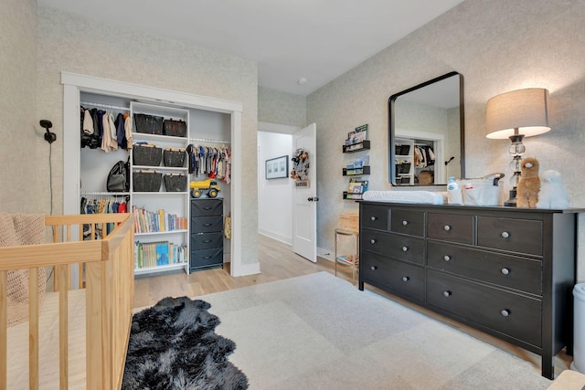 bedroom with a closet, a crib, baseboards, and wood finished floors