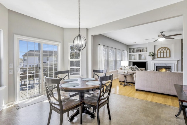 dining room with a healthy amount of sunlight, built in features, a fireplace, and ceiling fan with notable chandelier