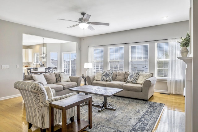 living room featuring baseboards, a ceiling fan, a healthy amount of sunlight, and light wood-type flooring