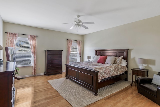 bedroom featuring baseboards, ceiling fan, multiple windows, and light wood-style flooring