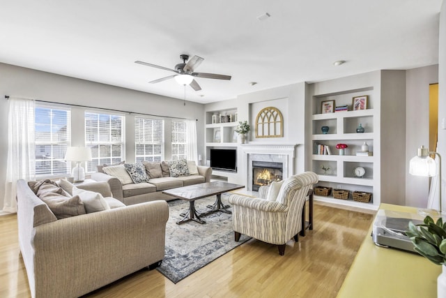 living area with a ceiling fan, light wood-style floors, built in features, and a fireplace
