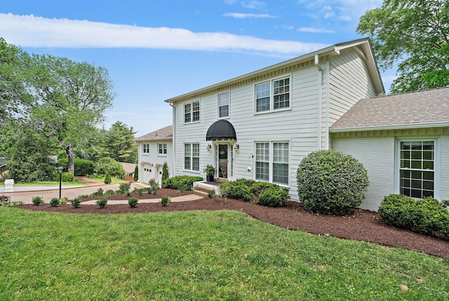 colonial home featuring a garage, a shingled roof, brick siding, and a front yard