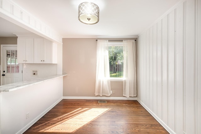 unfurnished dining area with visible vents, baseboards, plenty of natural light, and wood finished floors