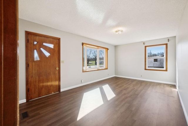 foyer entrance with dark wood-style flooring, a textured ceiling, visible vents, and baseboards