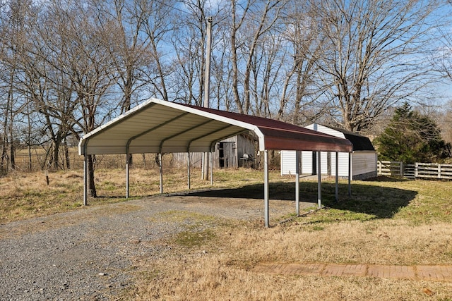 view of parking with gravel driveway, fence, and a carport