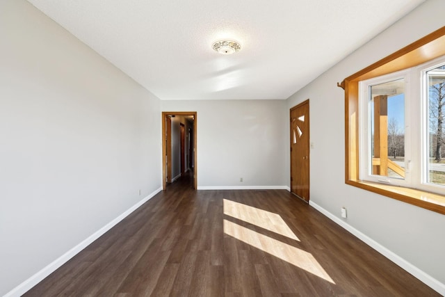 spare room featuring baseboards and dark wood finished floors