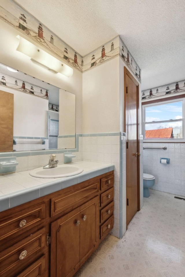 bathroom with toilet, a textured ceiling, tile walls, and vanity
