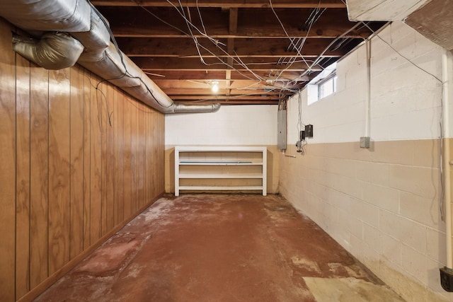 basement featuring wooden walls, concrete block wall, and electric panel