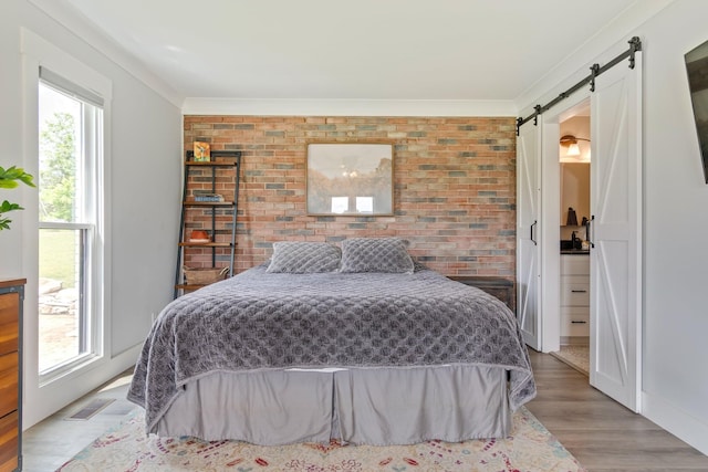 bedroom with a barn door, brick wall, light wood-type flooring, visible vents, and ornamental molding